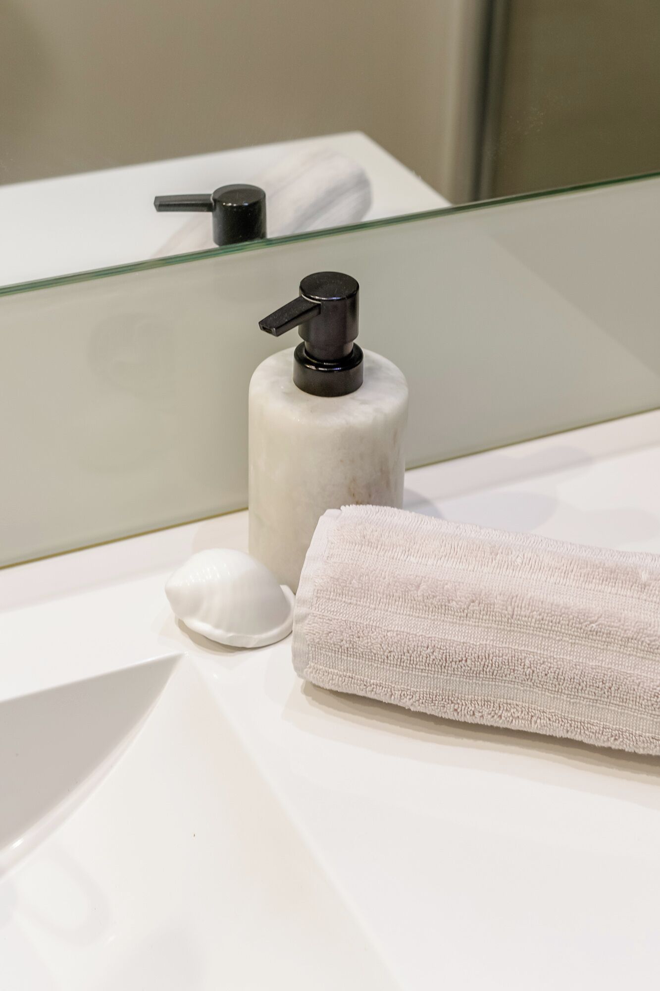 A bathroom with a white sink, a soap dispenser, a towel, and a glass shower enclosure.