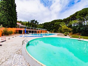 Ein Pool mit einer Steindeck, einem überdachten Sitzbereich und Bäumen und Hügeln im Hintergrund.