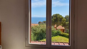 Een kamer met een grote glazen schuifdeur die uitkomt op een balkon met uitzicht op zee en groen.