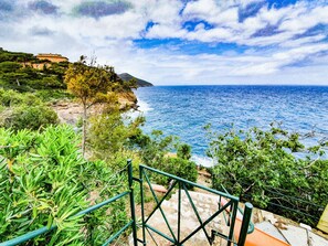 A coastal landscape with a staircase leading down to the beach, overlooking the sea and a building on a hill.