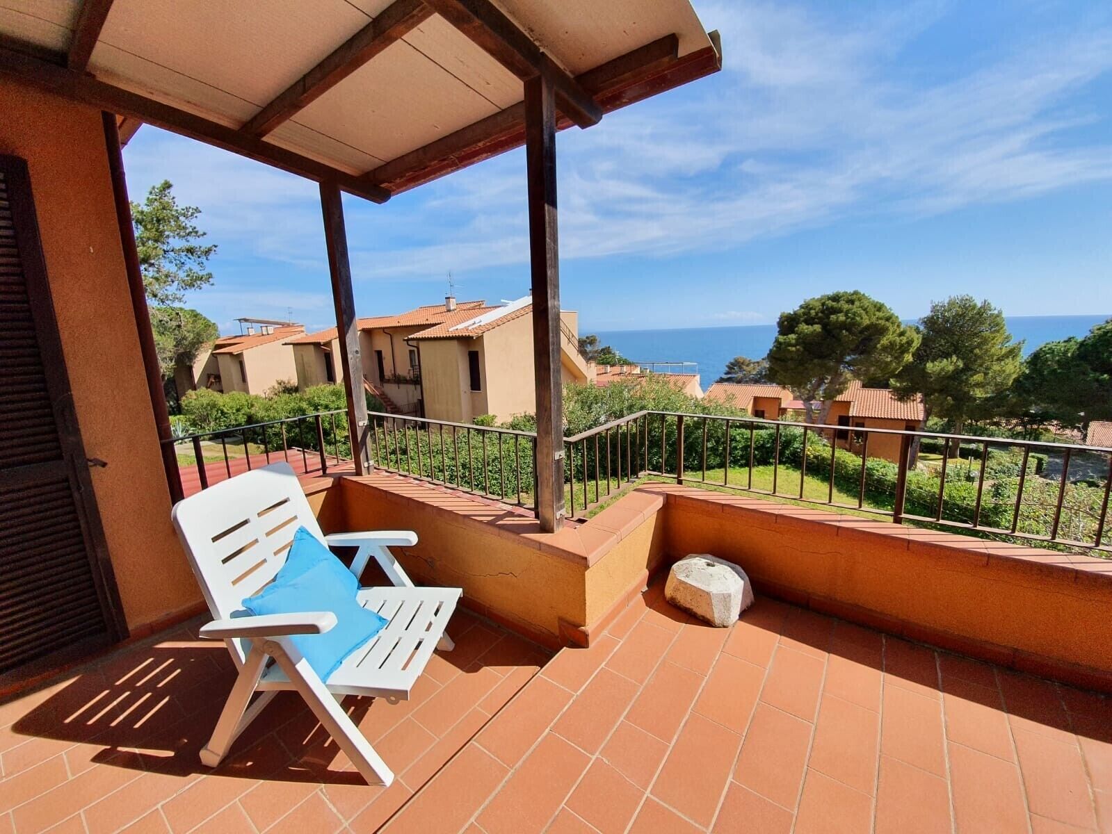 A balcony with a white chair, a tiled floor, and a view of houses and the sea.