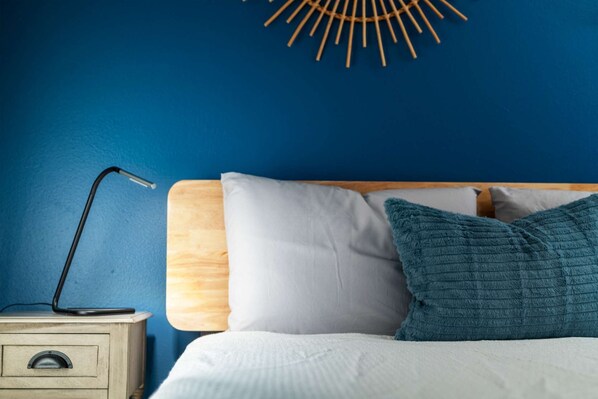 A bed with white and teal pillows, a wooden headboard, and a bedside table with a lamp.