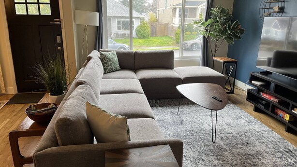 A living room with a sectional sofa, a coffee table, a TV, and a bookshelf. - Heart of Alberta Arts District, Pet Friendly, Walk to Alberta Park, Food, Art, and Drinks (Portland)
