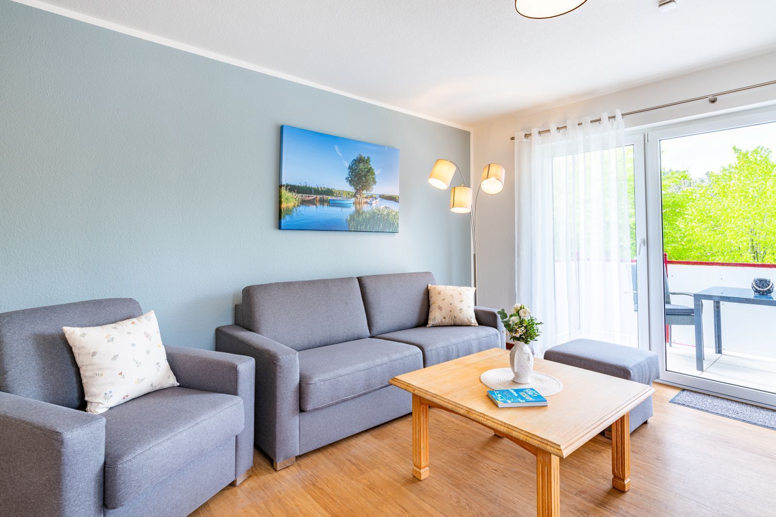 A modern living room with a grey sofa set, a wooden coffee table, and a painting of a lake.