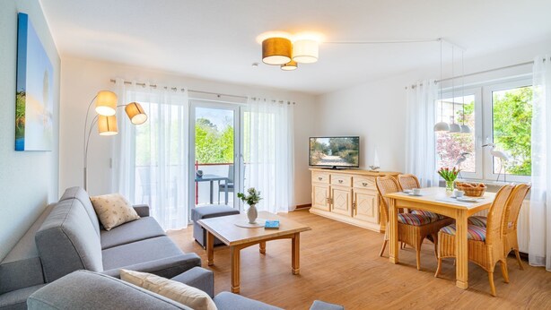 Un salon moderne comprenant un canapé, une table à manger et des chaises, un téléviseur, et donnant sur un espace verdoyant.