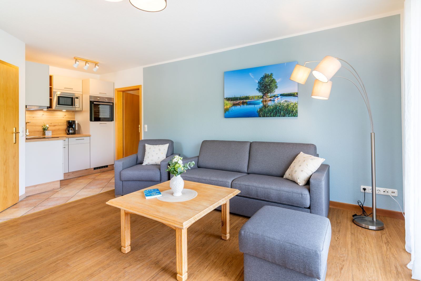 Un salon moderne avec un canapé gris, une table basse en bois et un tableau représentant un lac.