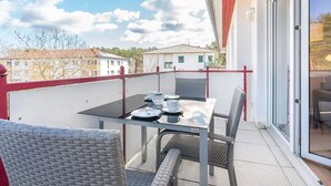 Un balcon avec une table dressée pour deux personnes, des chaises en osier et une porte vitrée donnant sur une pièce.