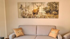 Un canapé gris avec deux coussins marron, un tableau représentant un cerf accroché au mur et une prise de courant sur le mur.