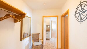 Un couloir avec un fauteuil en osier, un miroir et un décor mural représentant une boussole.