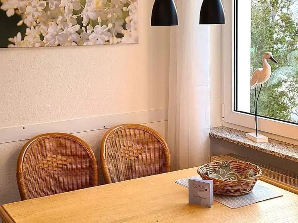 Un coin repas avec des chaises en osier, une table en bois, un panier et une fenêtre donnant sur un oiseau.
