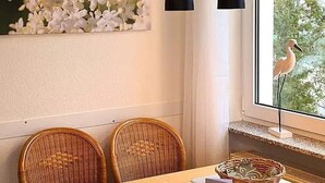 Un coin repas avec des chaises en osier, une table en bois, un panier et une fenêtre donnant sur un oiseau.