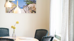 Un coin repas avec des chaises en osier, une table ronde, un vase de fleurs et des luminaires suspendus.