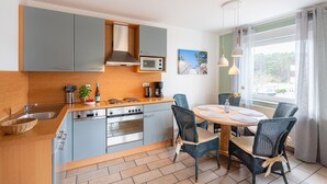 Une cuisine moderne avec des meubles gris, un four encastré et un coin repas comprenant des chaises en osier et une table ronde.