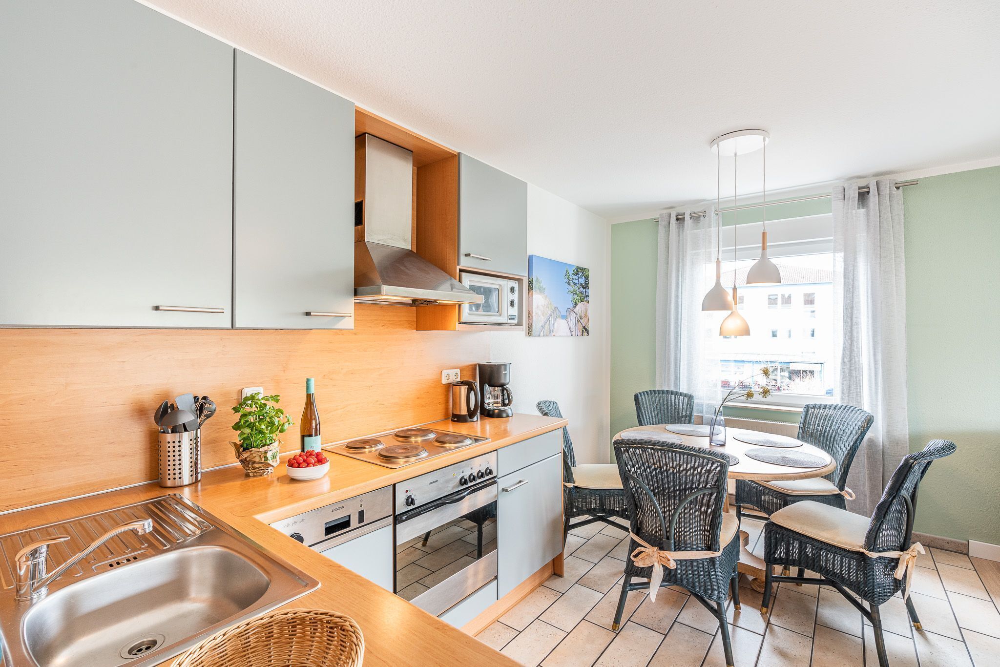 Cocina compacta con pileta, estufa y horno, comedor con mesa y sillas, y ventana con cortinas.