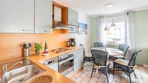 Une cuisine compacte comprenant un évier, une cuisinière et un four, un coin repas avec une table et des chaises, et une fenêtre avec des rideaux.
