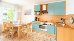 A modern kitchen with teal cabinets, a wooden dining table, and chairs.