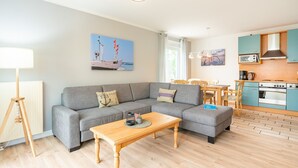 A modern living room with a grey sofa, wooden coffee table, and a kitchen area with blue cabinets and a stove.