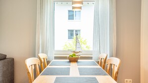 A dining area with a table set for four, surrounded by wooden chairs, a basket of apples, and a sailboat decoration.