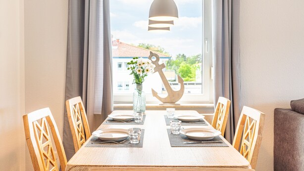 A dining table set for four with a view of a building and greenery outside. - Meerliebe - Stern FeWo Strandstraße (Karlshagen)