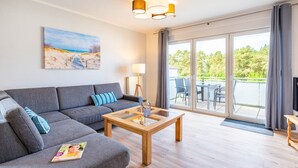 A modern living room with a grey sofa, a wooden coffee table, and a painting of a beach scene. - Meerliebe - Stern FeWo Strandstraße (Karlshagen)