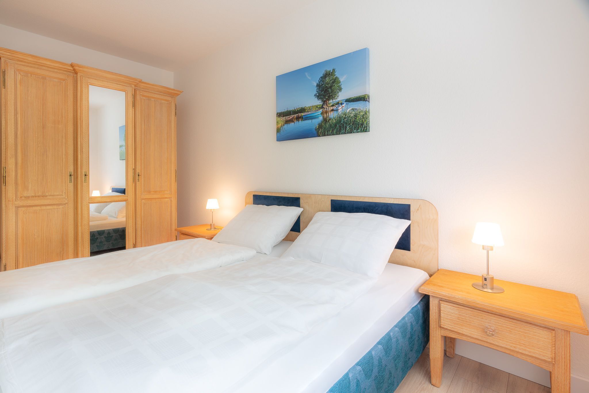 A bedroom with a bed, wooden wardrobe, bedside tables, and a wall-mounted painting.