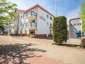 En bygning med flere etager, hvid facade og røde detaljer, med altaner og et skilt med tekst.
