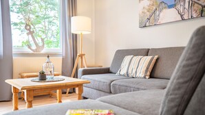 A living room with a grey sofa, a wooden coffee table with a plant, a lamp, and a magazine on the sofa. - Seewind - Stern FeWo Strandstrasse (Karlshagen)