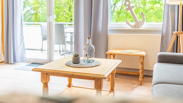 A room with a wooden table, a small potted plant, and a view of greenery outside. - Seewind - Stern FeWo Strandstrasse (Karlshagen)