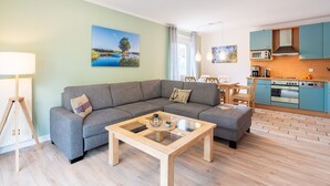 Een moderne woonkamer met een grijze bank, een salontafel met glazen blad en een houten vloer.