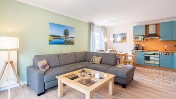 Ein modernes Wohnzimmer mit grauem Sofa, einem Couchtisch mit Glastischplatte und Holzboden.