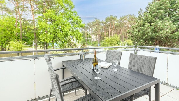 Een terras buiten met een houten tafel, twee stoelen, een fles wijn en twee glazen.