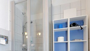 Une salle de bain avec une douche à parois de verre, des toilettes blanches et des étagères de rangement bleues.