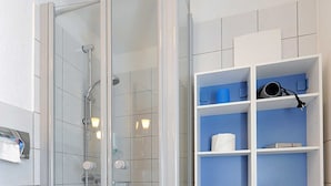 Une salle de bain avec une douche à parois de verre, des toilettes blanches et des étagères de rangement bleues.