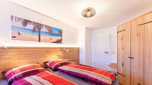 A bedroom with a bed, a wooden wardrobe, a door, and a wall-mounted picture of a beach scene.