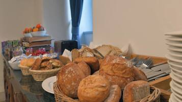 A buffet table with various breads and pastries, a bowl of tomatoes, and condiments.