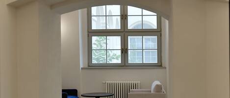 Una zona de recepción con suelo de baldosas, una ventana con vistas, un radiador y un sofá.