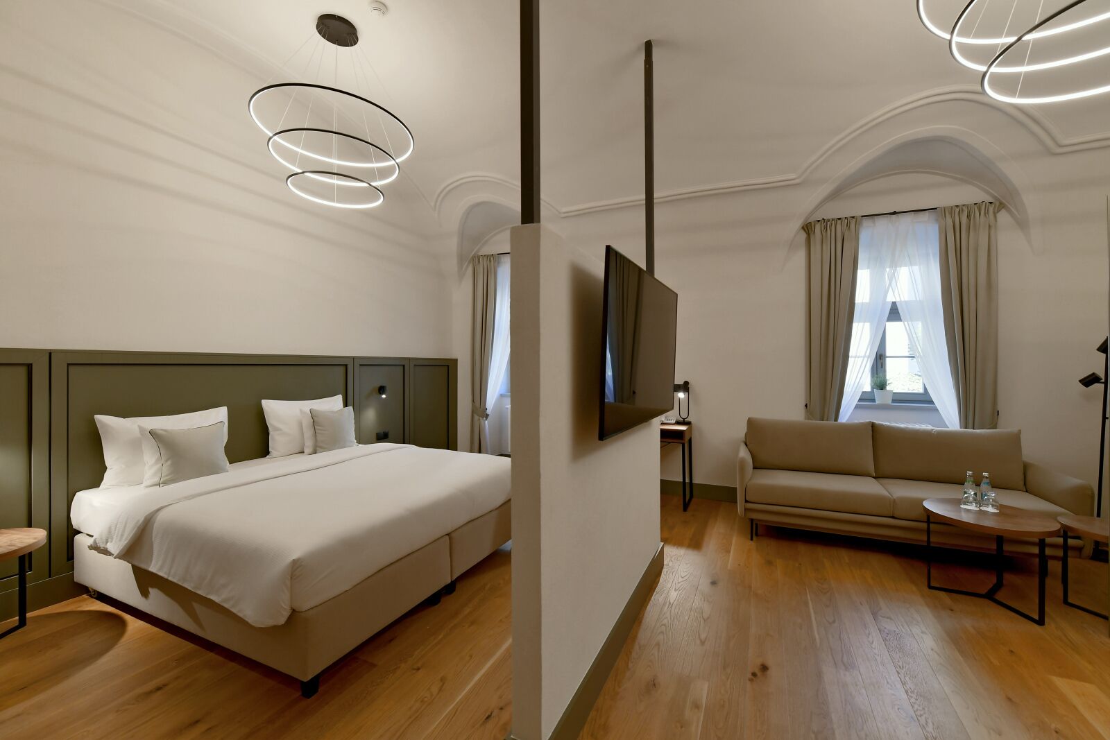 A hotel room with a bed, a sofa, a TV, and a wooden floor.