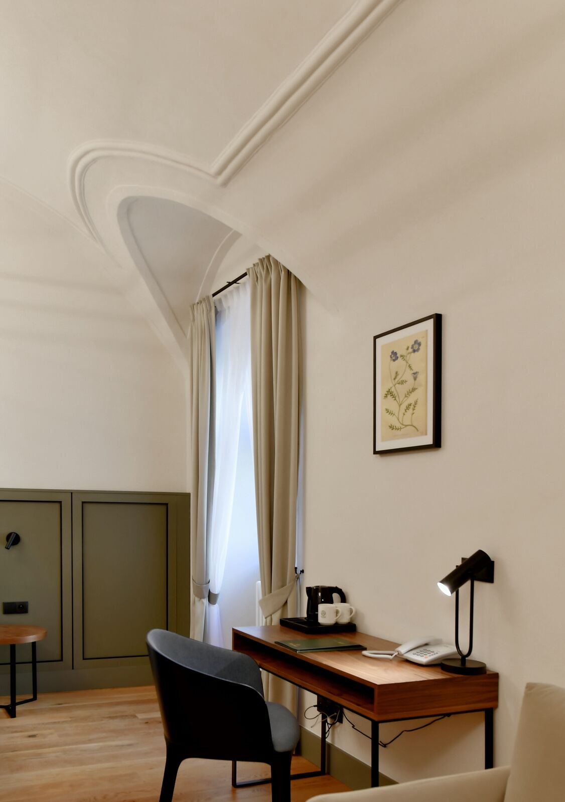 A room with a desk, chair, and a small table with a kettle and cups.