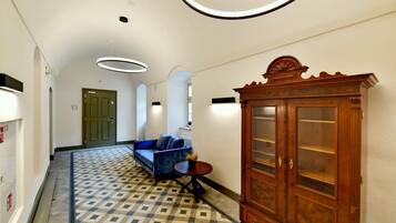 A hallway with a patterned floor, a blue sofa, a wooden cabinet, and a green door.