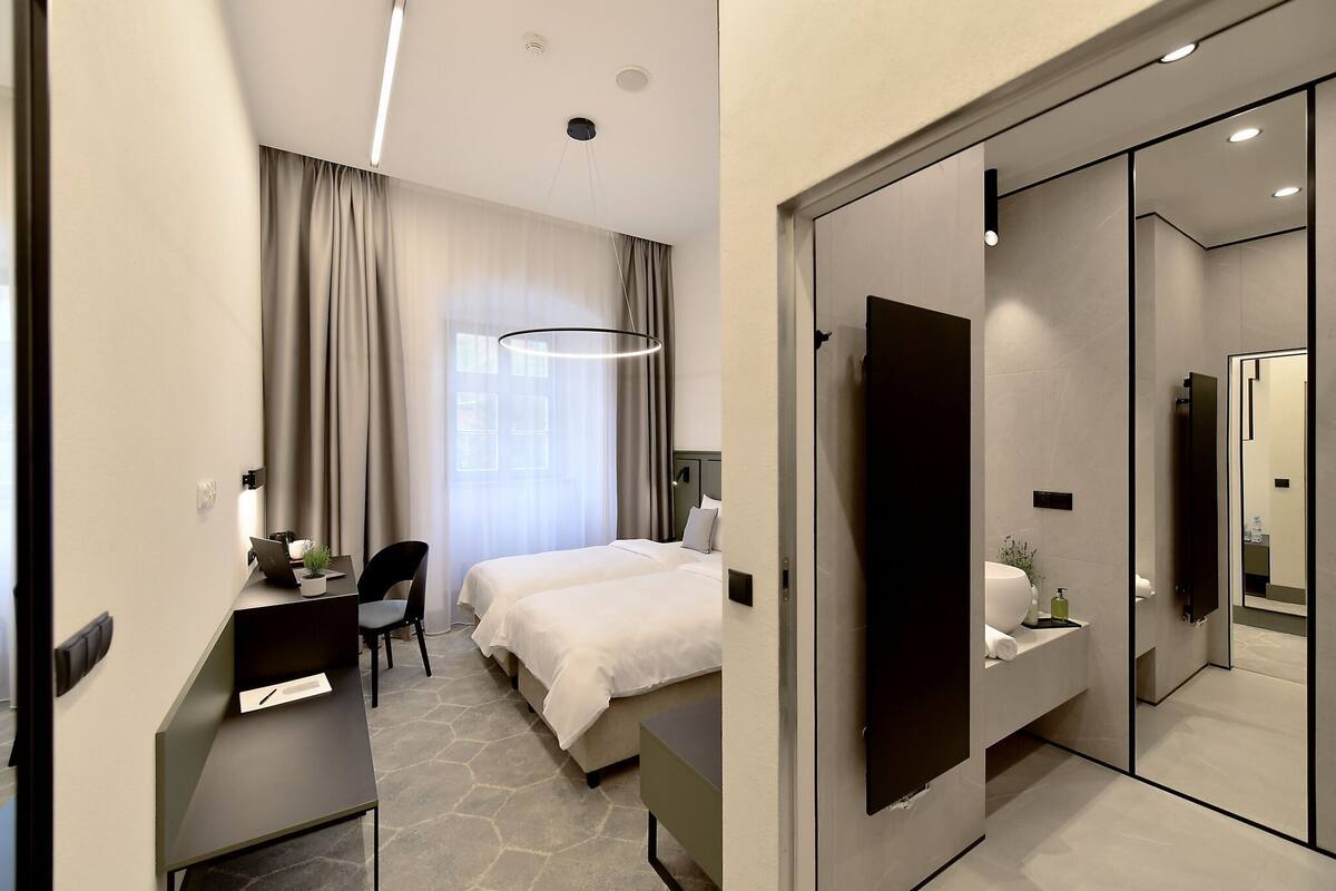 A hotel room with a bed, desk, chair, and a large mirror.