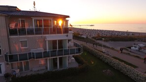 A two-story building with a balcony, a view of the beach, and a pier in the background. - Wohnung 1 und 2 - Strandresidenz-kühlungsborn (Kühlungsborn)