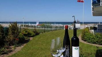 A table with two wine bottles and a glass, a flag, and a view of the sea and beach.