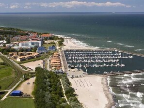 Vista aérea de una zona costera con un puerto deportivo, playa y edificios.