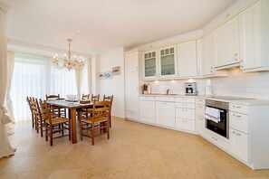 Une cuisine avec des meubles blancs, une table à manger avec des chaises, un lustre et une cuisinière.