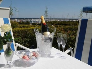 A table with a bottle of champagne, two glasses, and a bowl of snacks, set against a view of the sea and marina. - Kein Hüsung mit Kinderzimmer - Strandresidenz-kühlungsborn (Kühlungsborn)