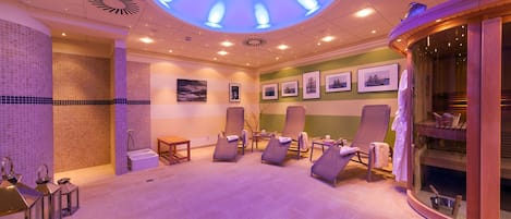 Une salle de spa avec un éclairage au plafond, des fauteuils inclinables, une table de massage et des tableaux encadrés accrochés au mur.