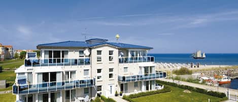 A multi-story hotel with balconies, a beach view, and a sailboat in the distance.
