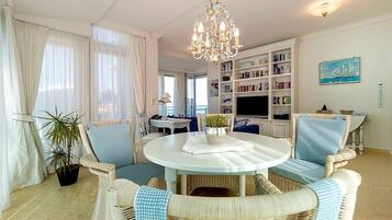 A living room with wicker furniture, a chandelier, a bookshelf, and a painting.
