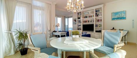 Un salon avec des meubles en osier, un lustre, une bibliothèque et un tableau.