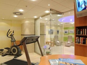 A room with a treadmill, a glass partition, a chair, and a bookshelf.